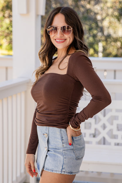 Woman wearing a brown long-sleeve top and denim shorts on a balcony.
