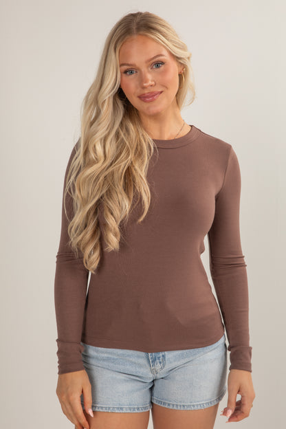 Woman wearing a brown long-sleeve top and denim shorts on a plain background