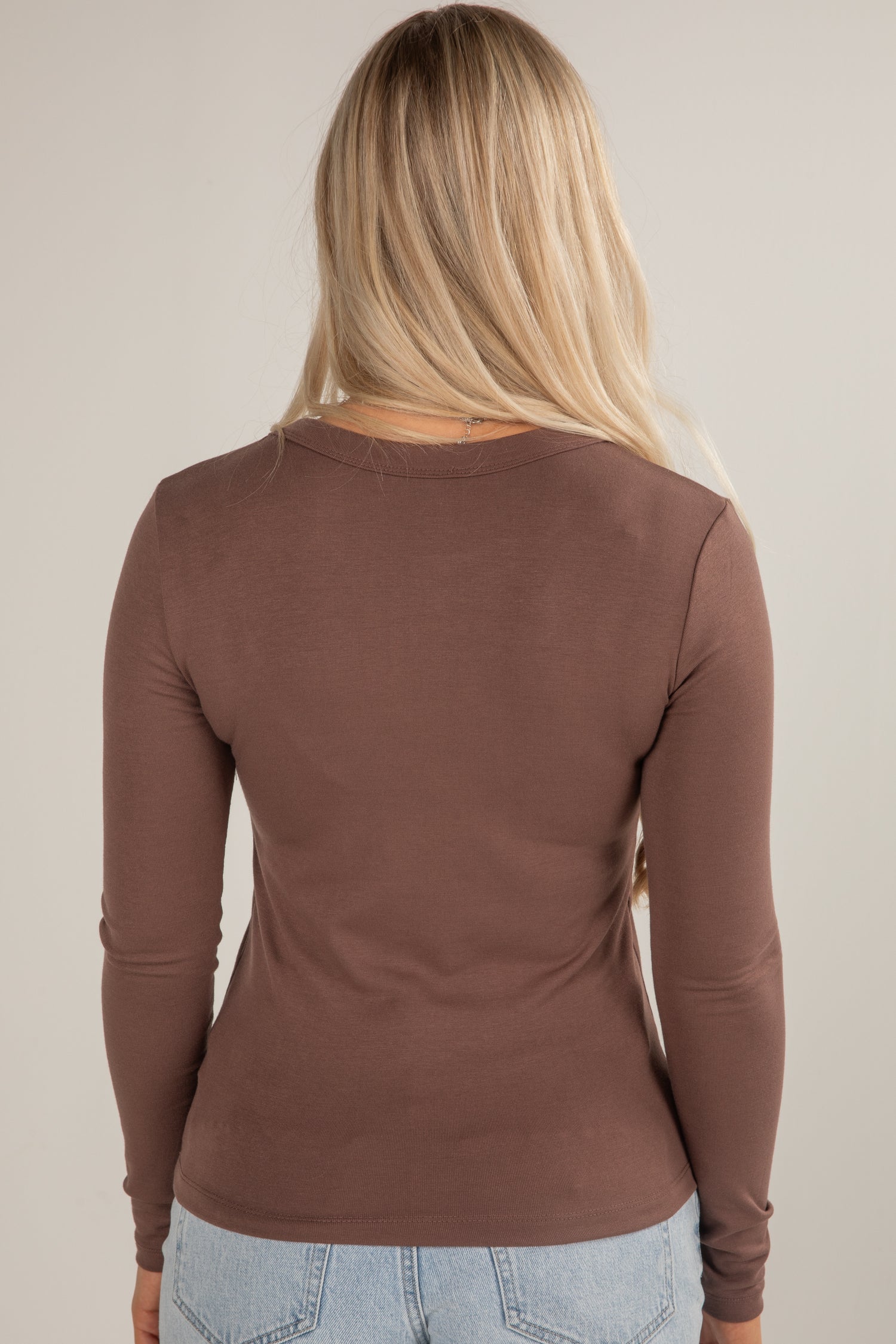 Person wearing a brown long-sleeve top against a beige background