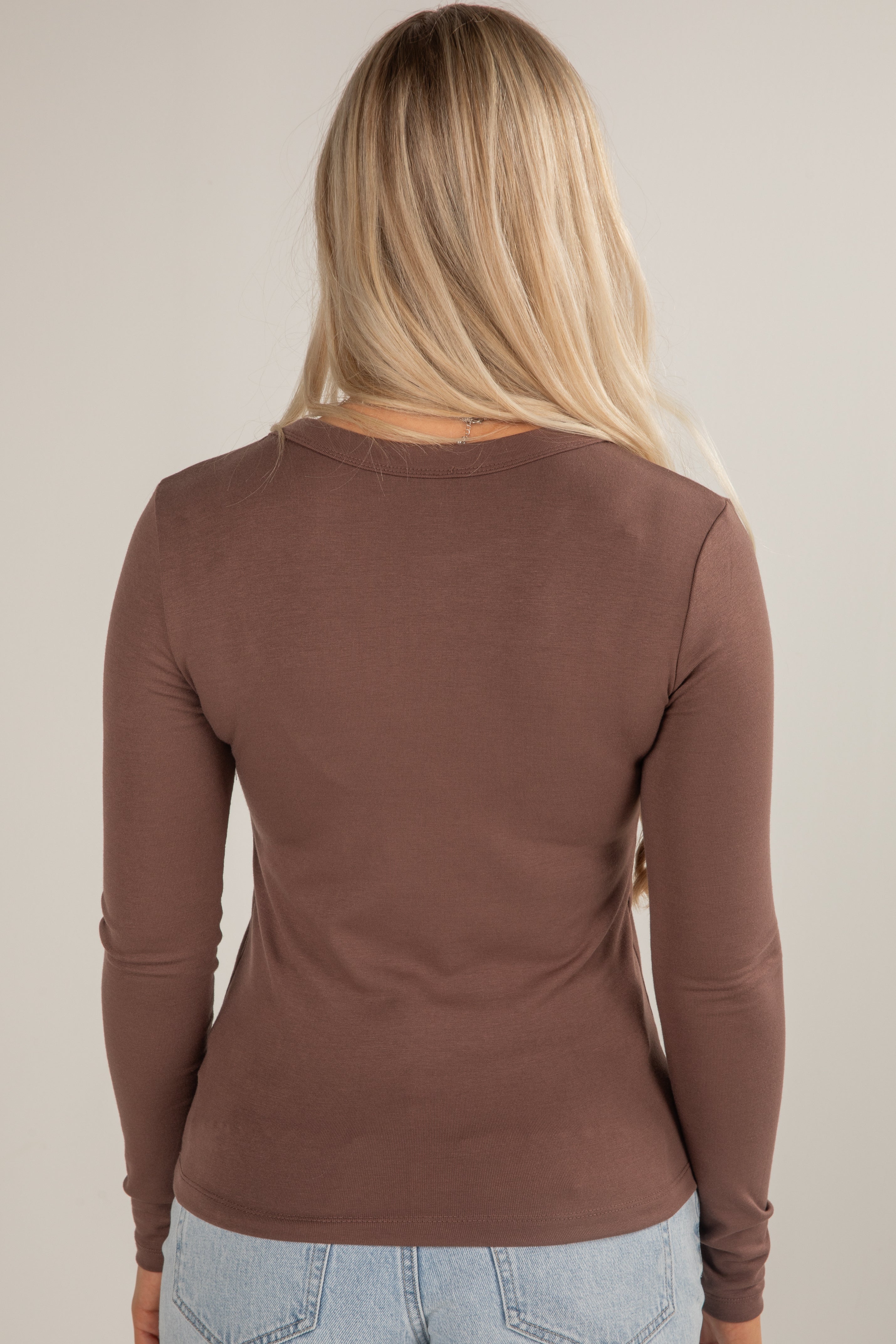 Person wearing a brown long-sleeve top against a beige background