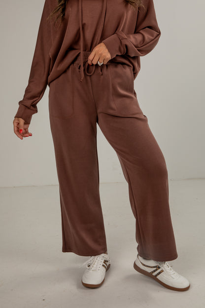 Person wearing a brown tracksuit with white sneakers on a plain background