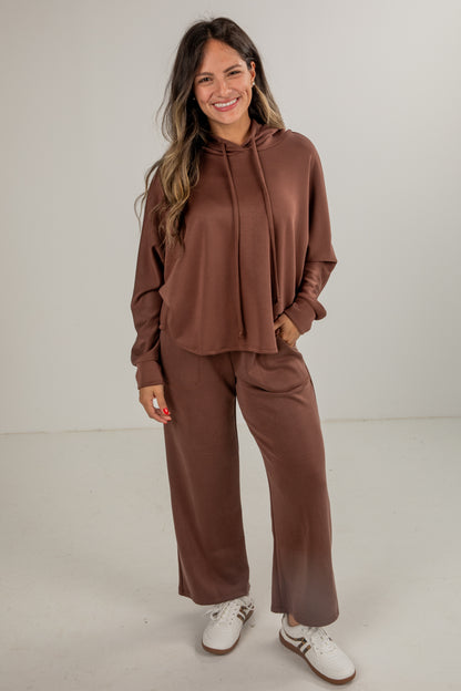 Woman wearing a brown tracksuit with white shoes on a plain background