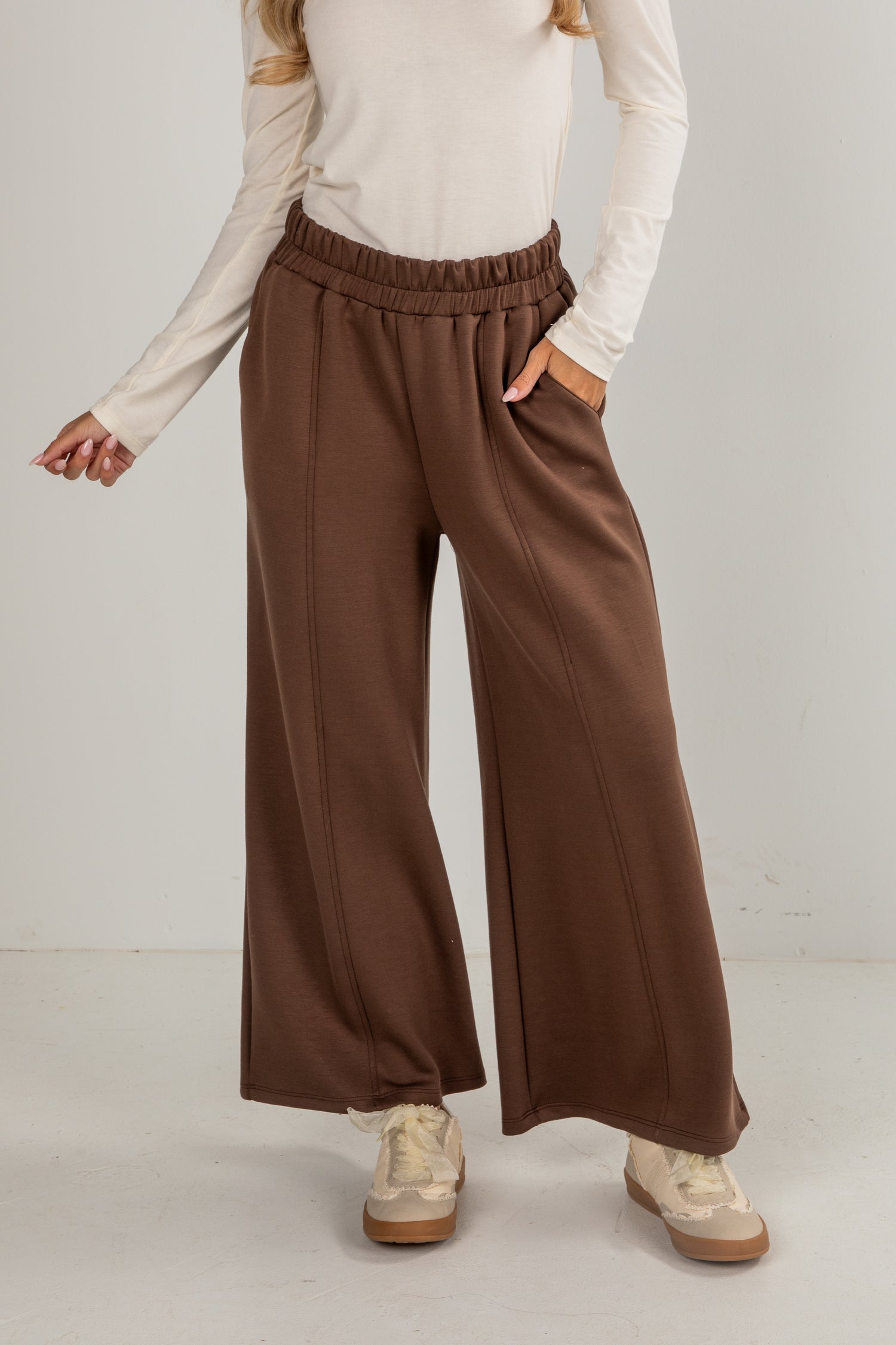 Person wearing brown wide-leg pants and a beige top on a plain background