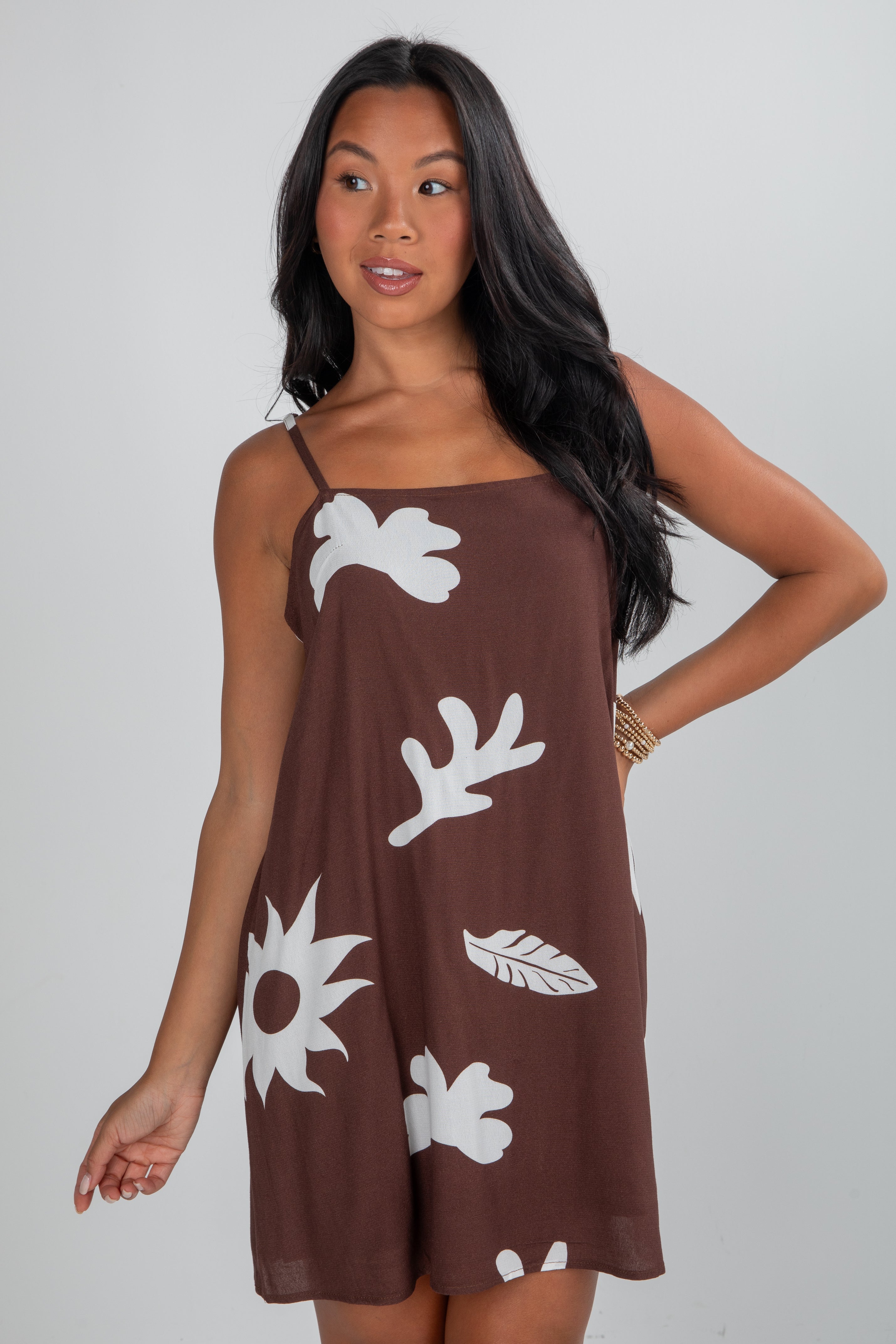 Woman wearing a brown dress with white floral patterns on a plain background