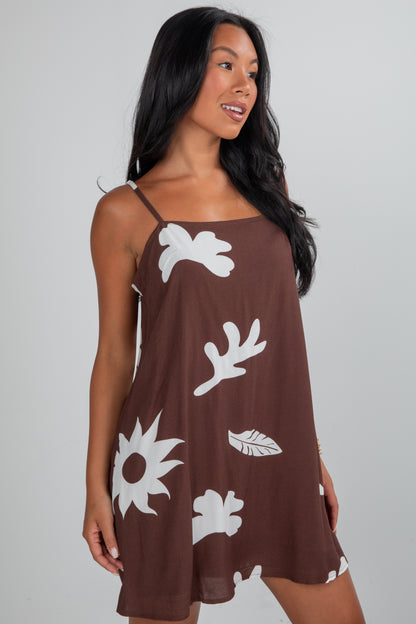 Woman wearing a brown dress with white floral patterns on a gray background