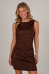 A smiling blonde woman wearing a sleeveless, knee-length brown faux-suede dress with side pockets, posed against a light gray studio background.