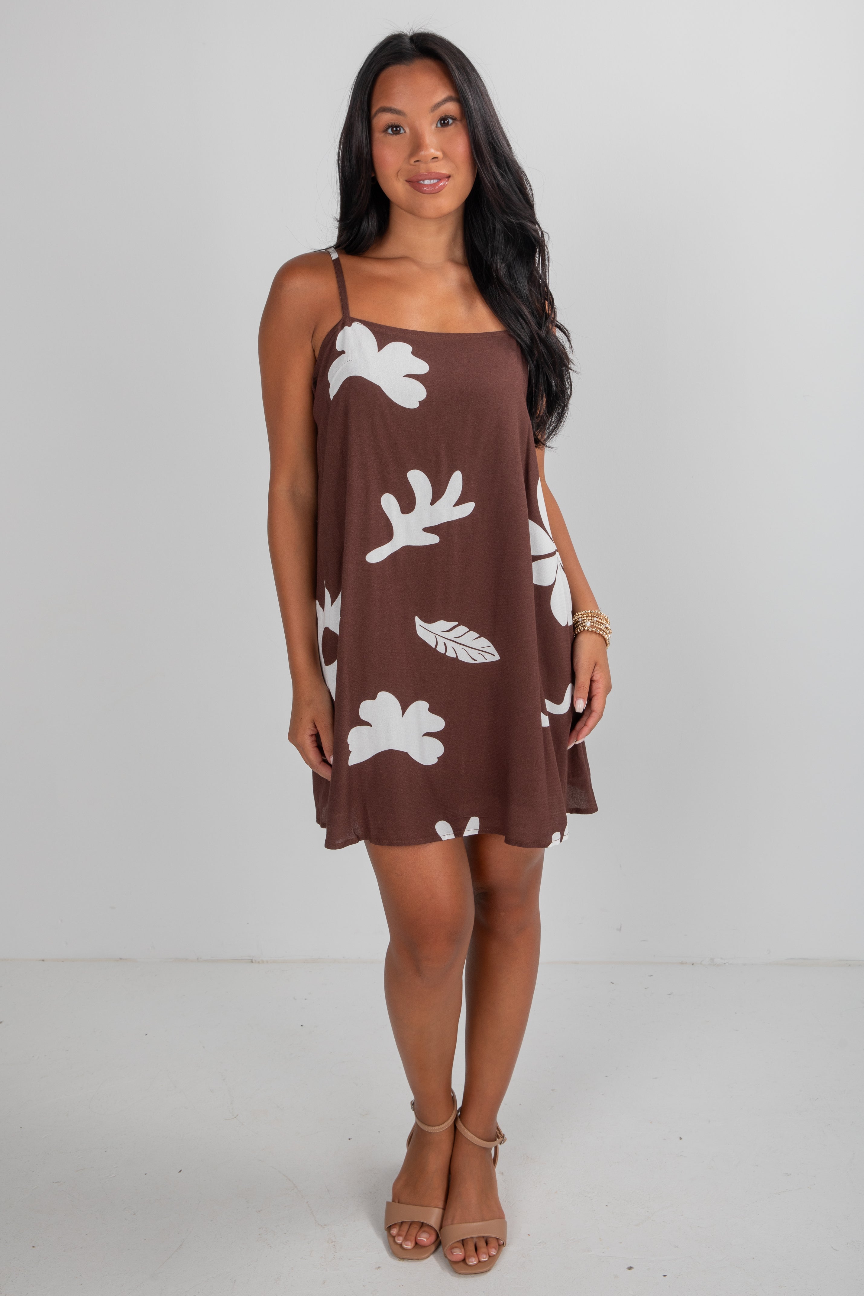 Woman wearing a brown dress with white floral patterns on a plain background