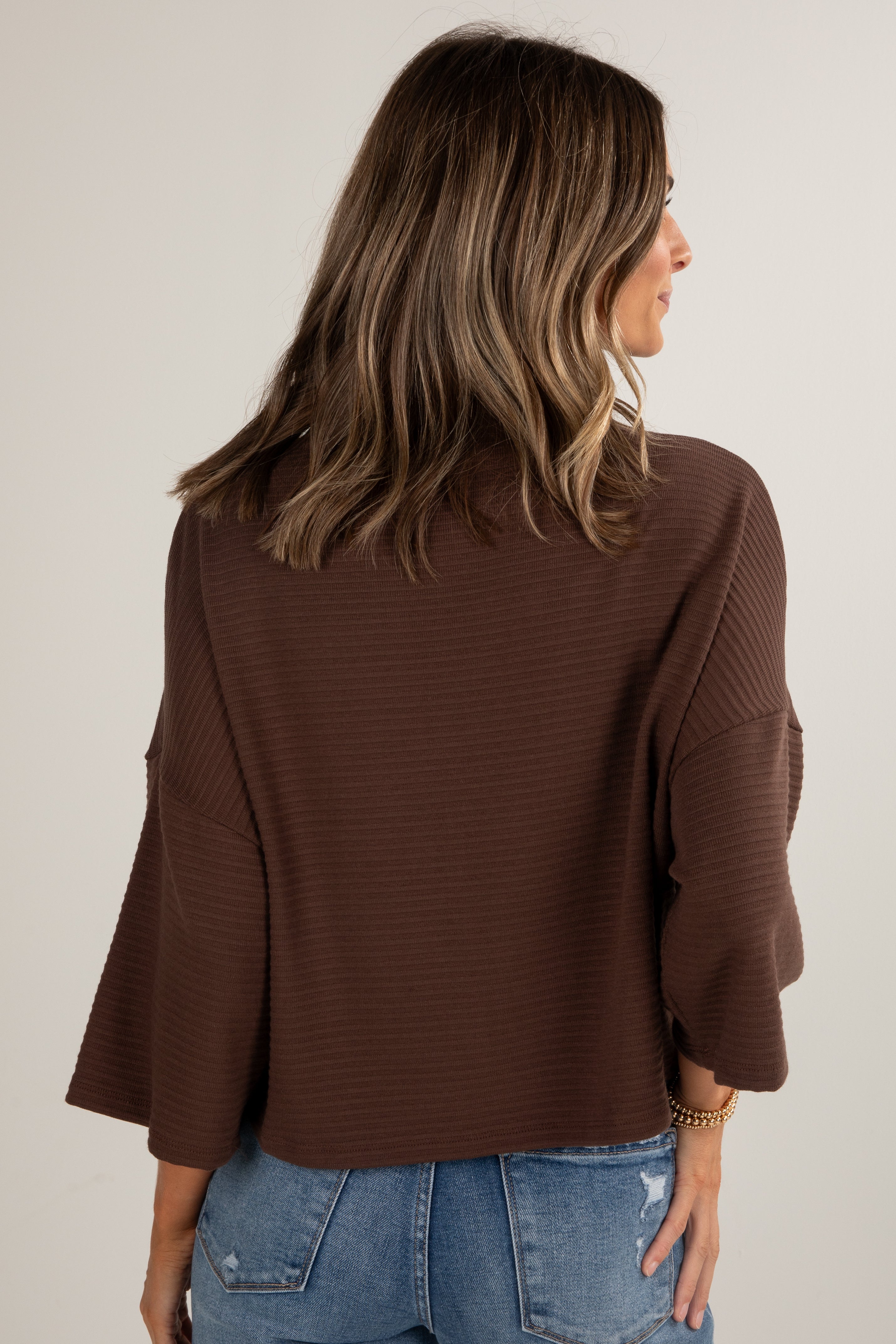 Woman wearing a brown sweater and blue jeans against a plain background