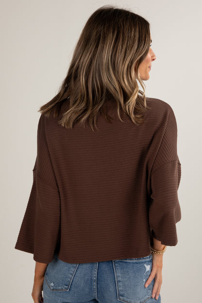 Woman wearing a brown sweater and blue jeans against a plain background