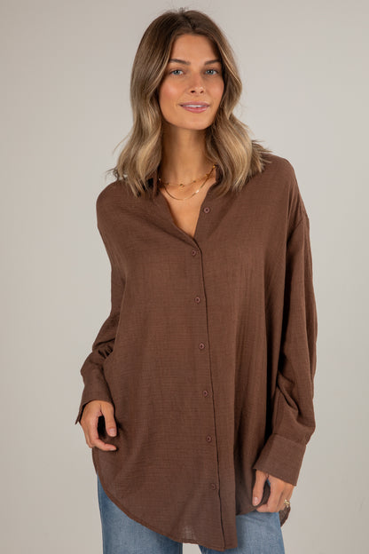 Woman wearing a brown button-up shirt against a plain background