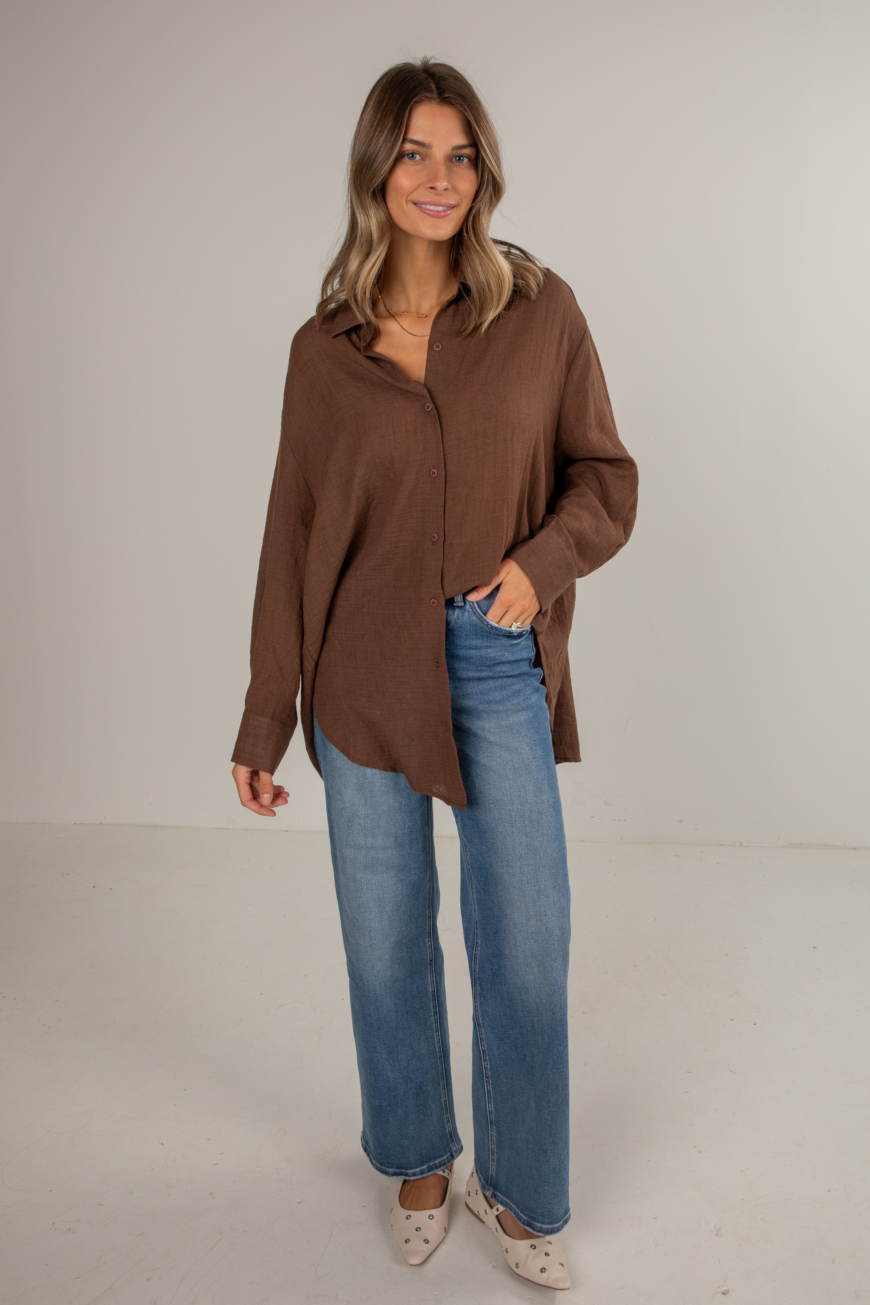 Woman wearing a brown shirt and blue jeans against a plain background