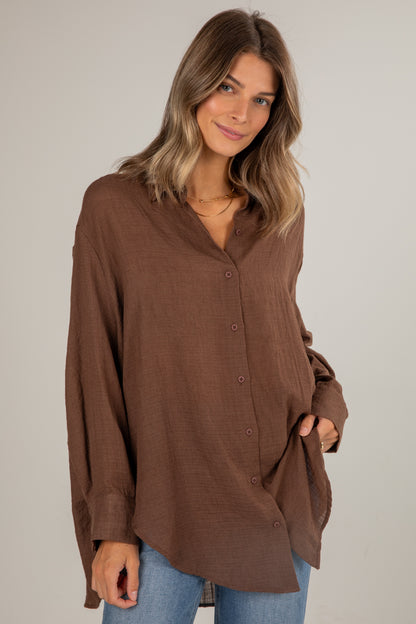 Woman wearing a brown button-up shirt against a plain background