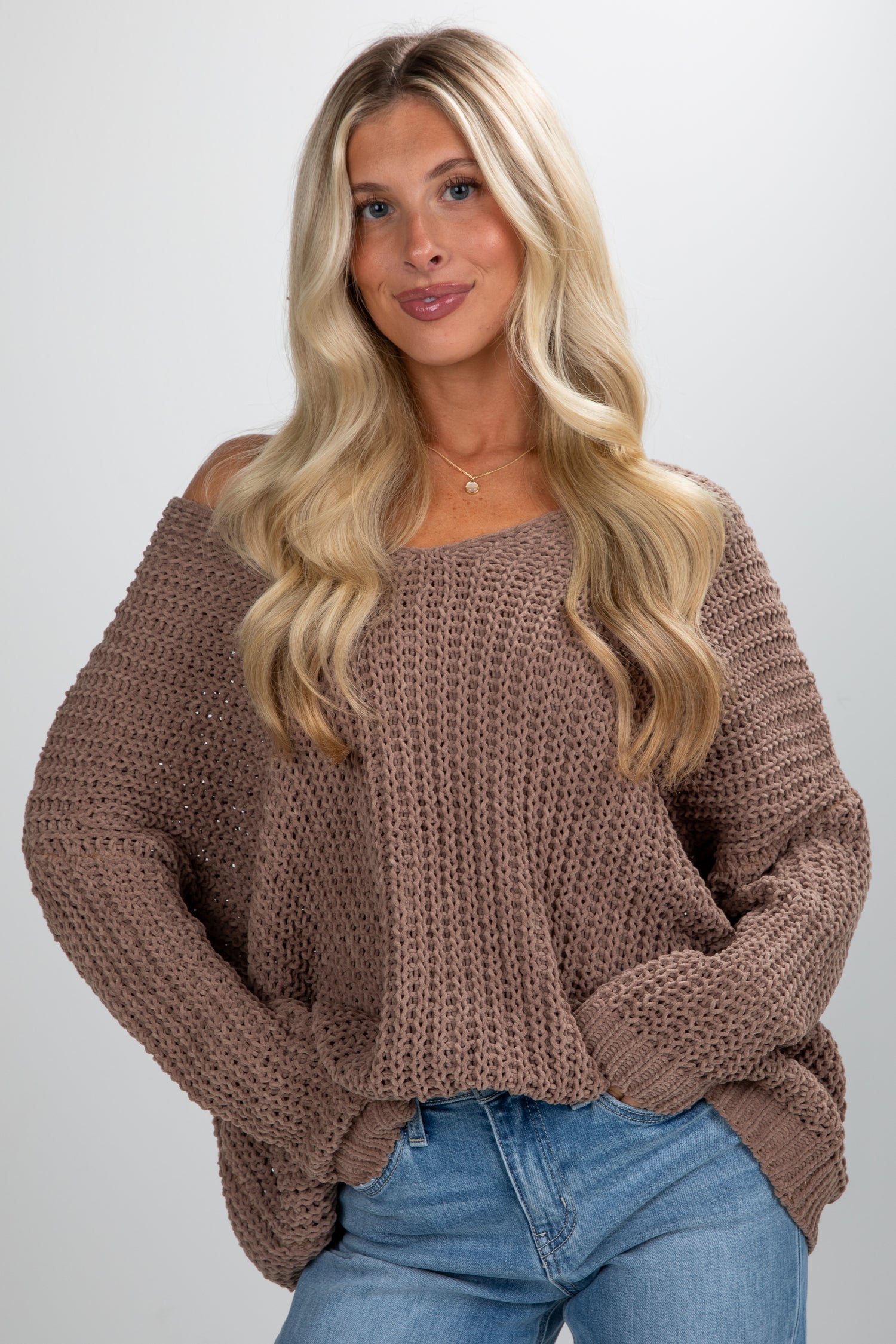 Woman wearing a brown chunky knit sweater and blue jeans on a plain background