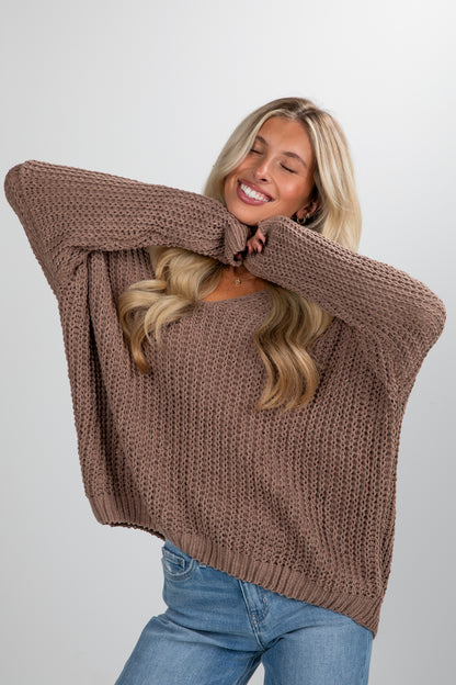Woman wearing a brown knitted sweater and blue jeans on a plain background