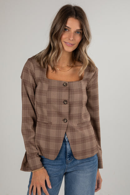 Woman wearing a brown plaid blazer and blue jeans on a plain background