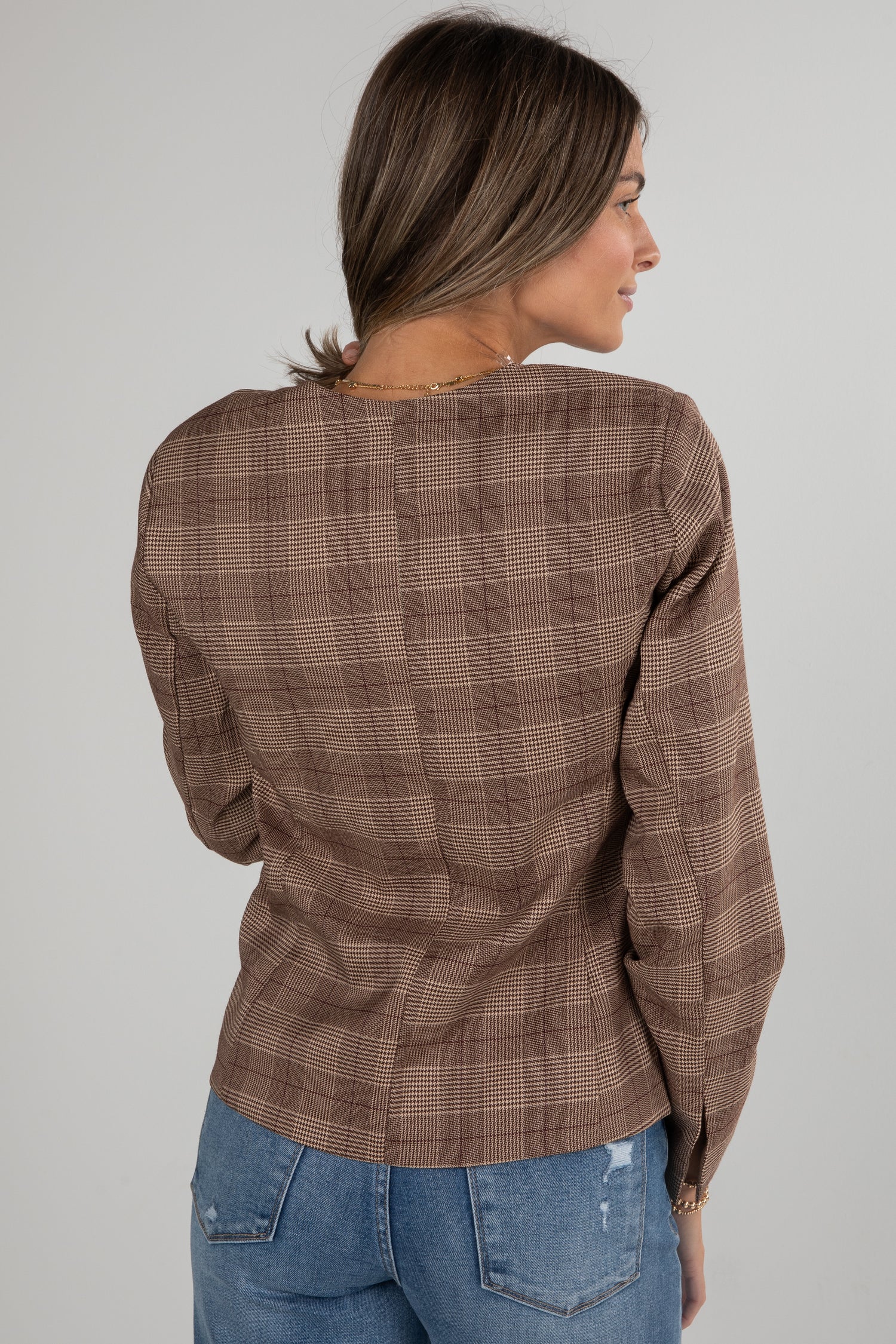 Woman wearing a brown plaid shirt and blue jeans on a plain background