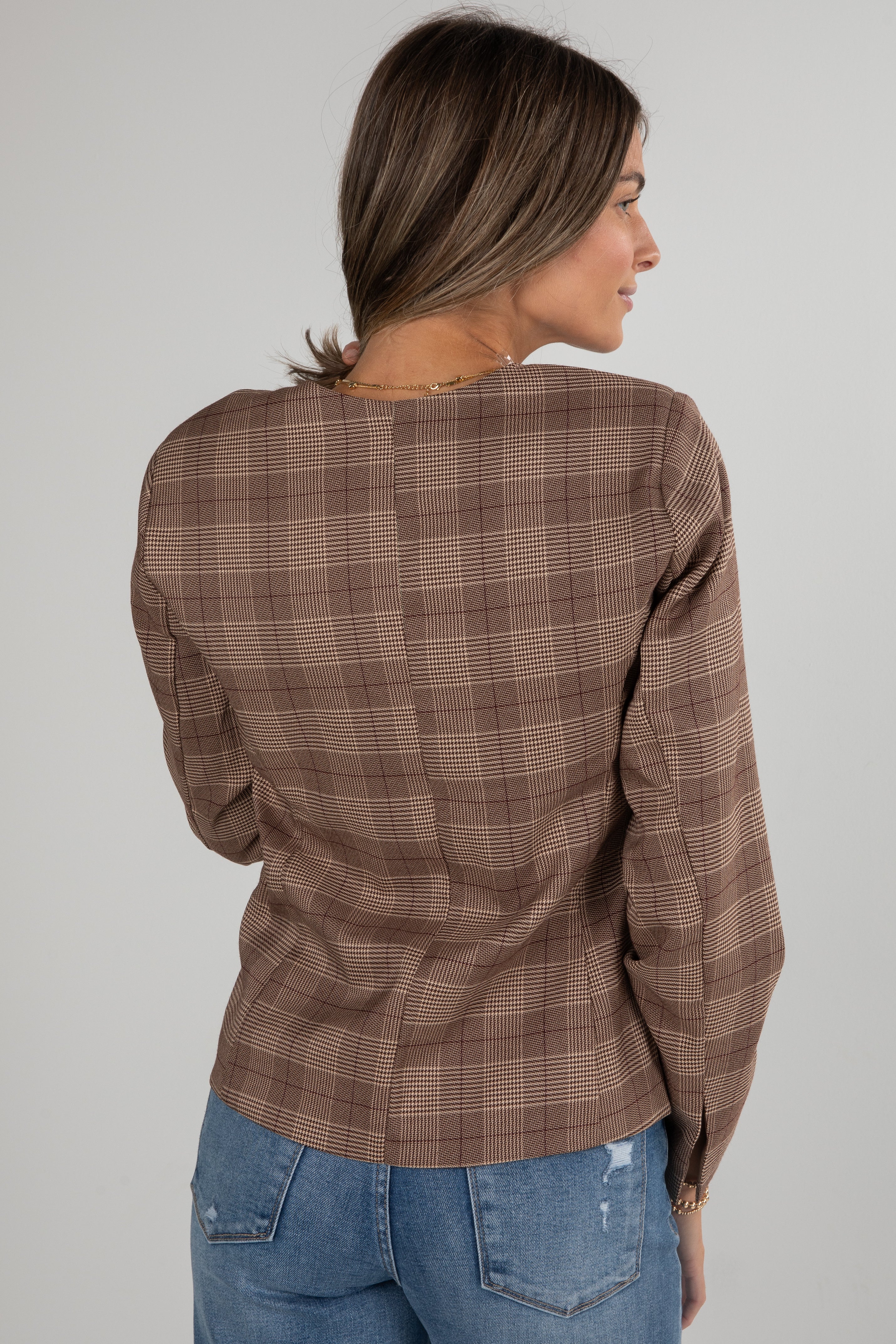Woman wearing a brown plaid shirt and blue jeans on a plain background