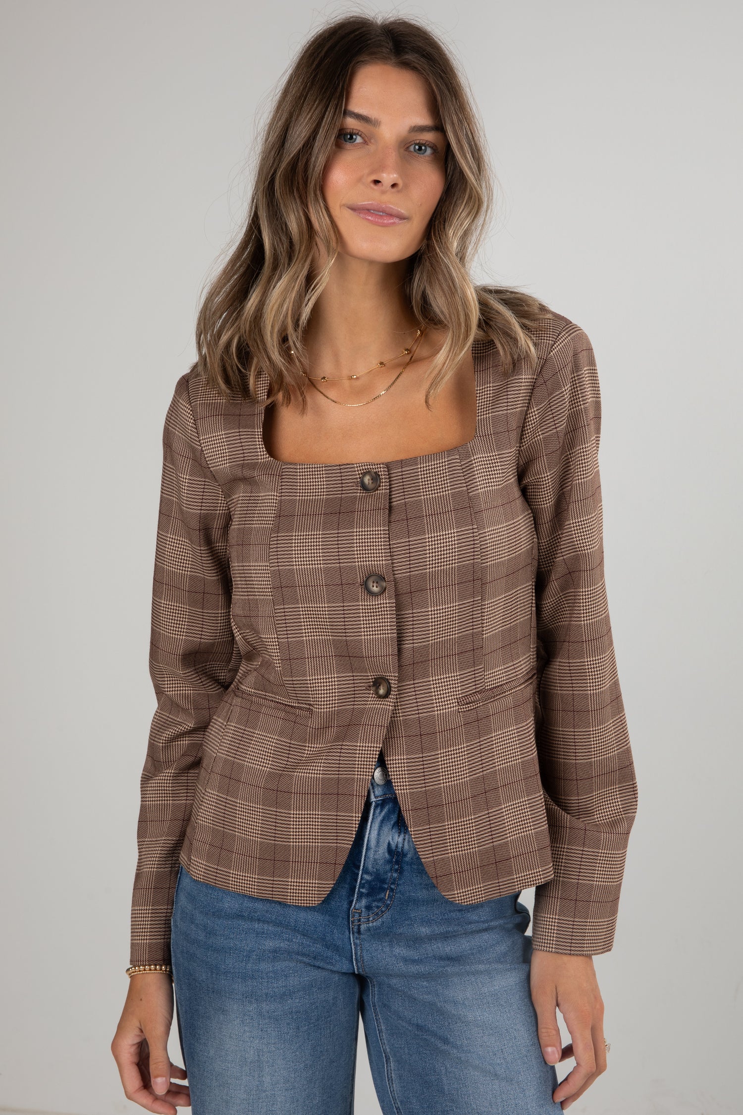 Woman wearing a brown plaid blazer and blue jeans against a plain background