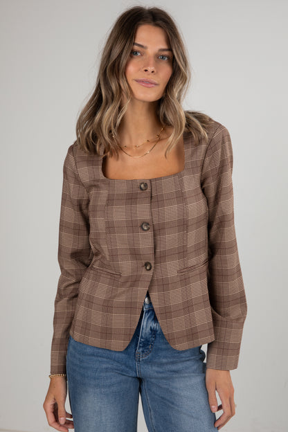 Woman wearing a brown plaid blazer and blue jeans against a plain background