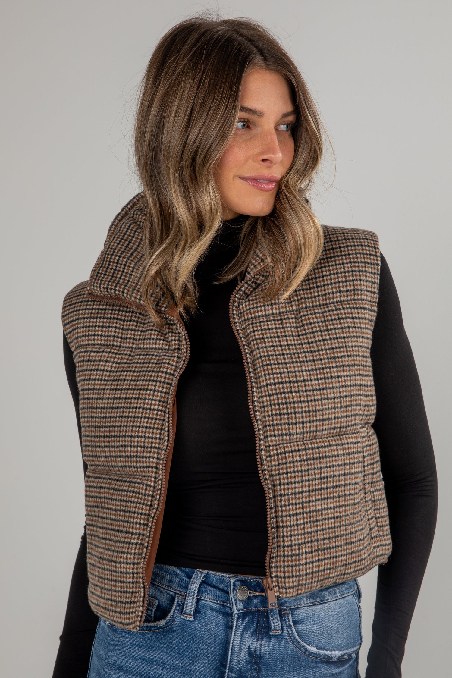 Woman wearing a plaid vest over a black top and blue jeans on a gray background