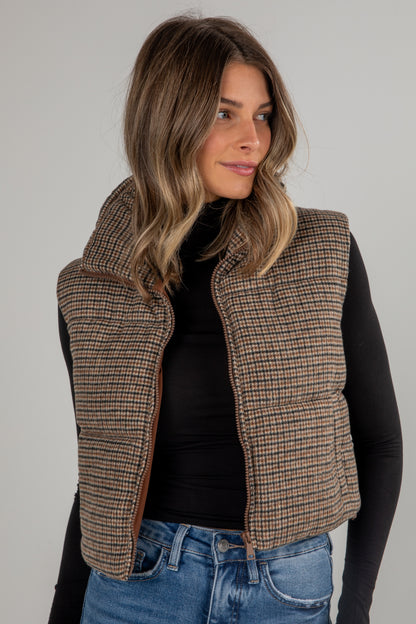 Woman wearing a plaid vest over a black top and blue jeans on a gray background