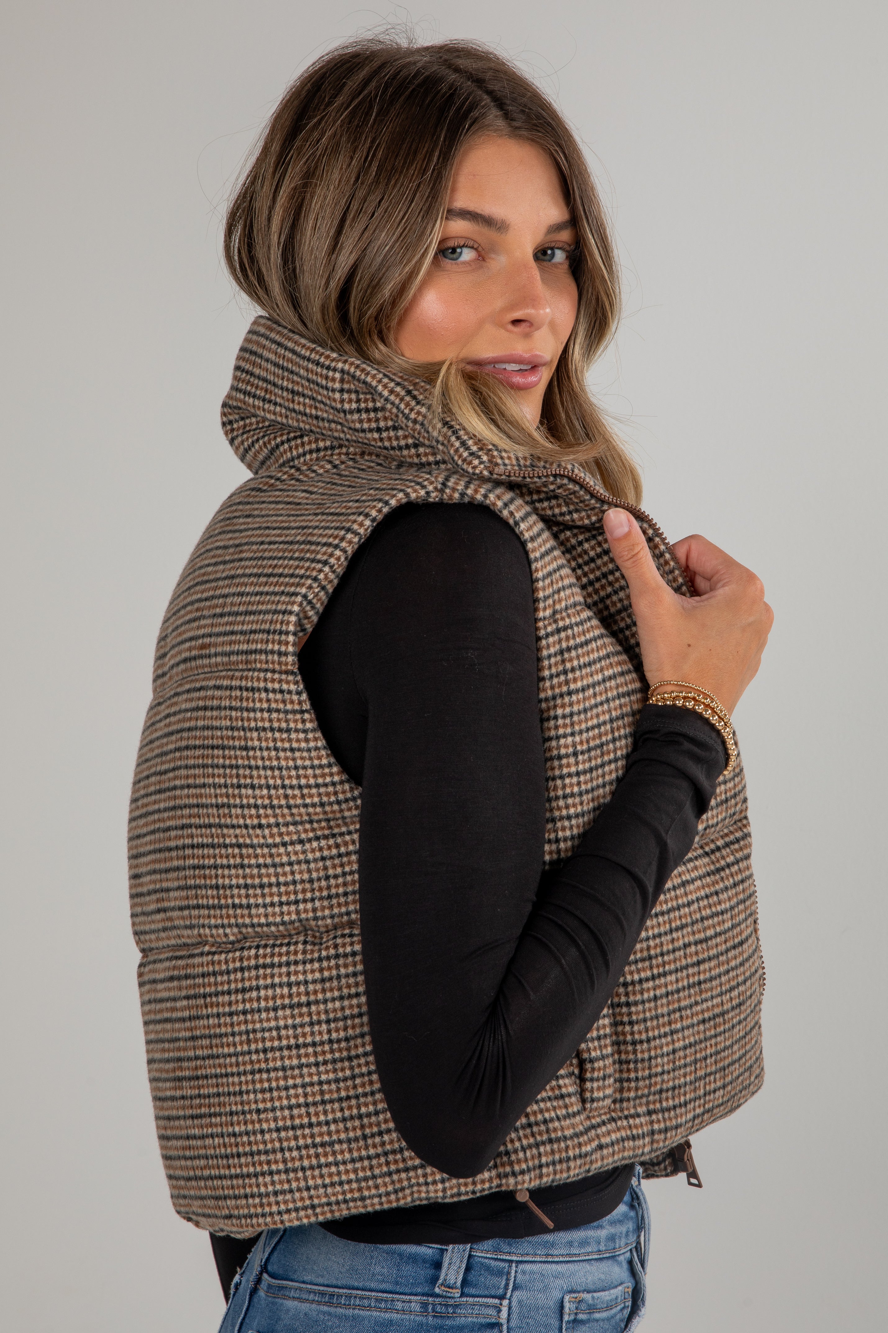 Woman wearing a plaid vest over a black long-sleeve shirt on a plain background