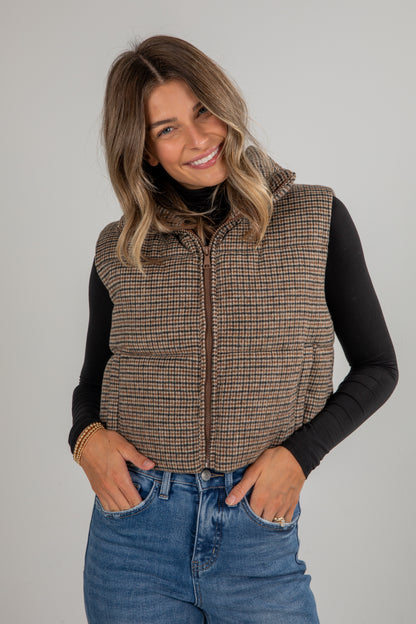 Woman wearing a plaid vest over a black long-sleeve shirt and blue jeans on a gray background