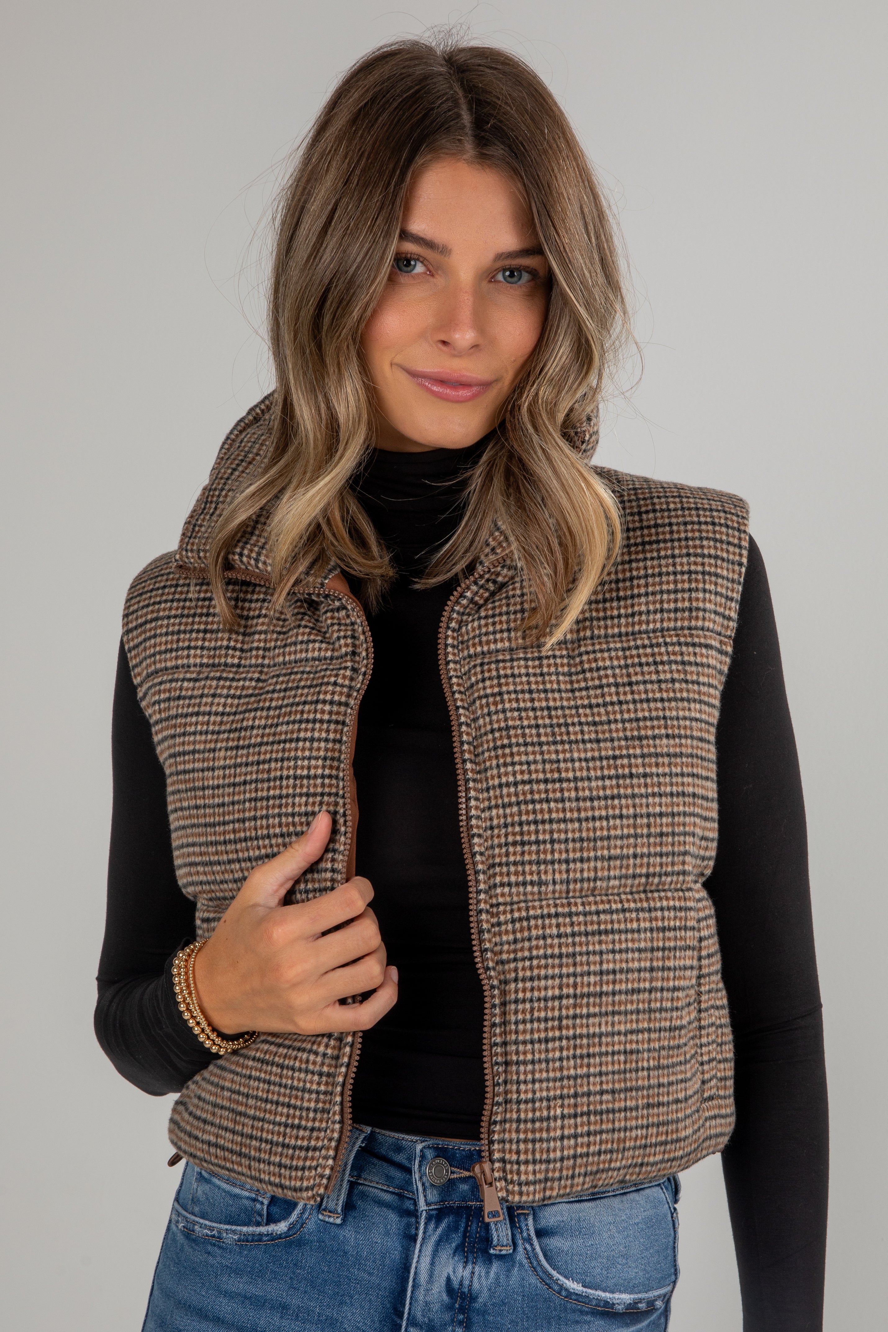 Woman wearing a plaid vest over a black top and blue jeans on a gray background