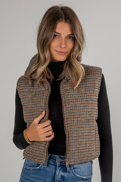 Woman wearing a plaid vest over a black top and blue jeans on a gray background