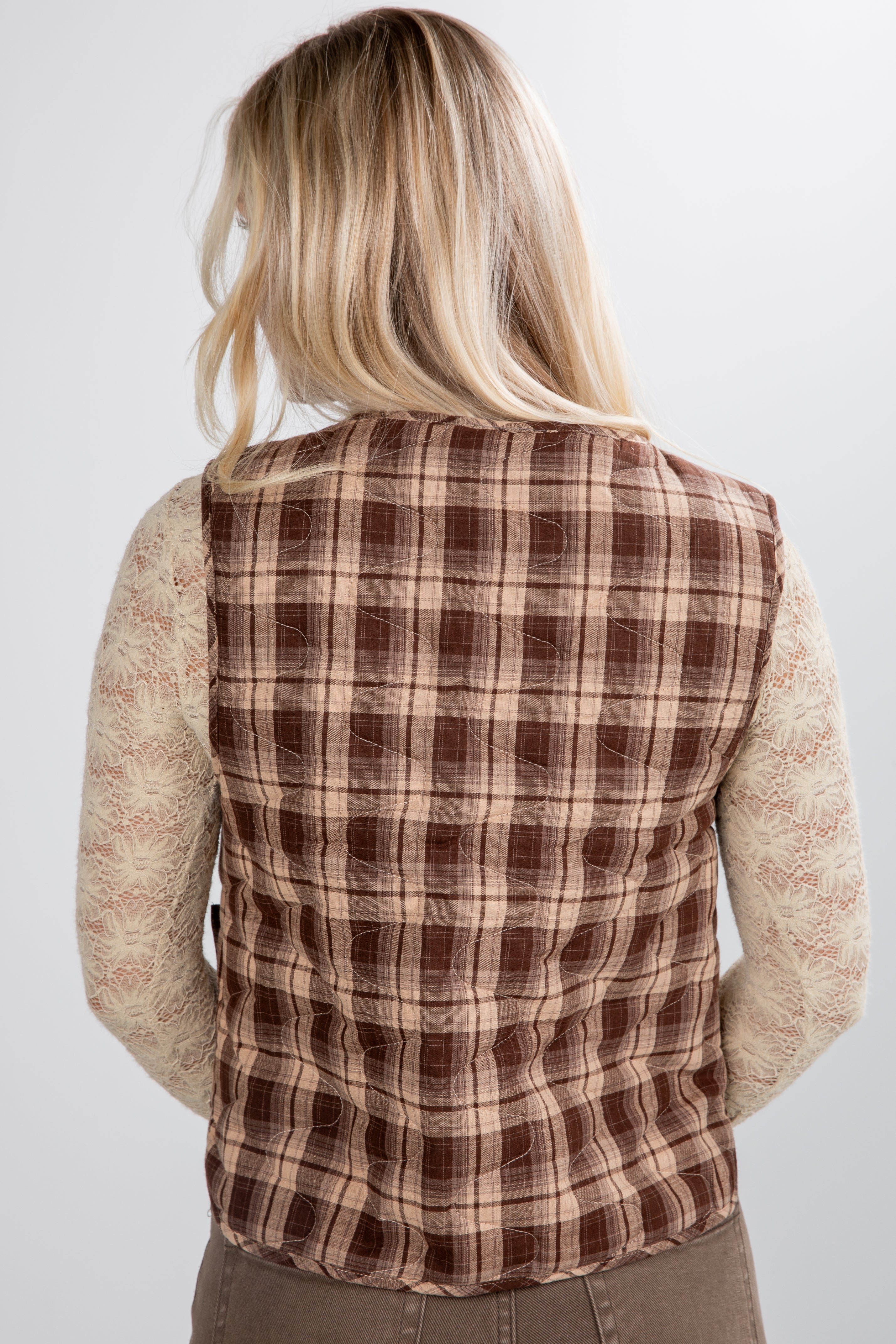 Person wearing a brown plaid vest over a beige sweater on a white background