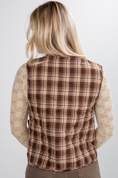Person wearing a brown plaid vest over a beige sweater on a white background