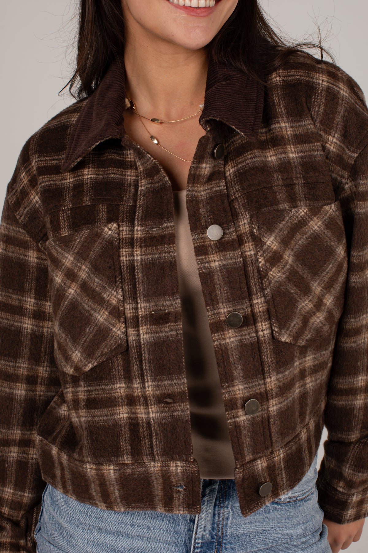 A cropped brown and beige plaid flannel jacket with a dark brown corduroy collar, worn by a model over a beige top and blue jeans.