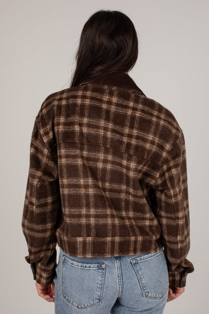 A person shown from the back wearing a brown and beige plaid flannel jacket with light blue jeans, photographed against a plain light gray studio background.