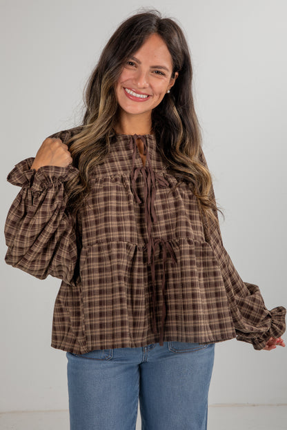 Woman wearing a brown plaid blouse with puffed sleeves against a white background