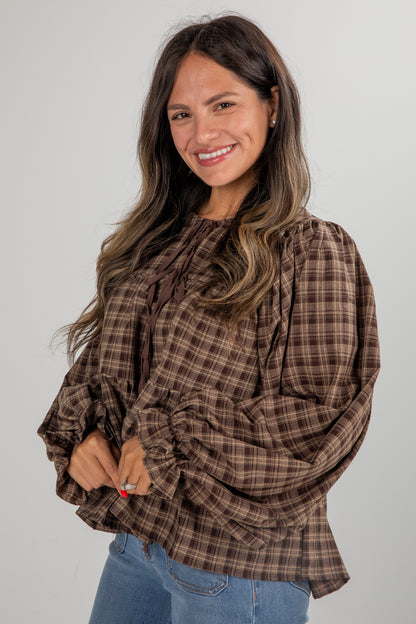 Woman wearing a brown plaid blouse with ruffled sleeves against a plain background