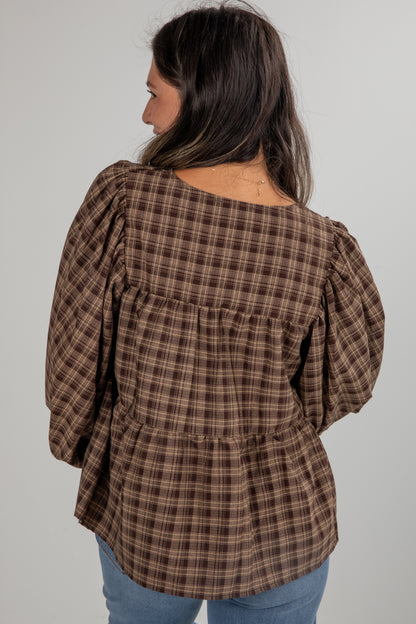 Woman wearing a brown plaid blouse with puffed sleeves on a plain background