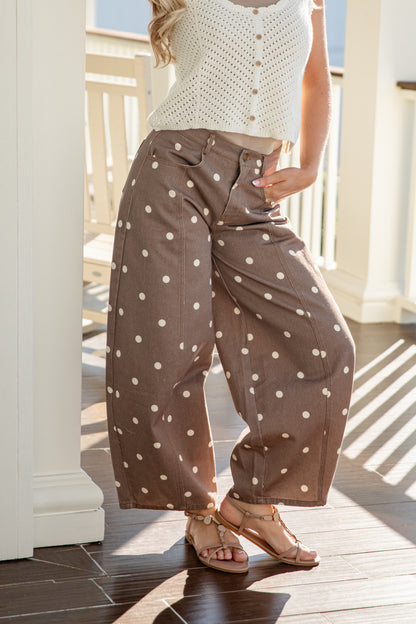 Person wearing a white sleeveless top and brown polka dot pants on a wooden deck.