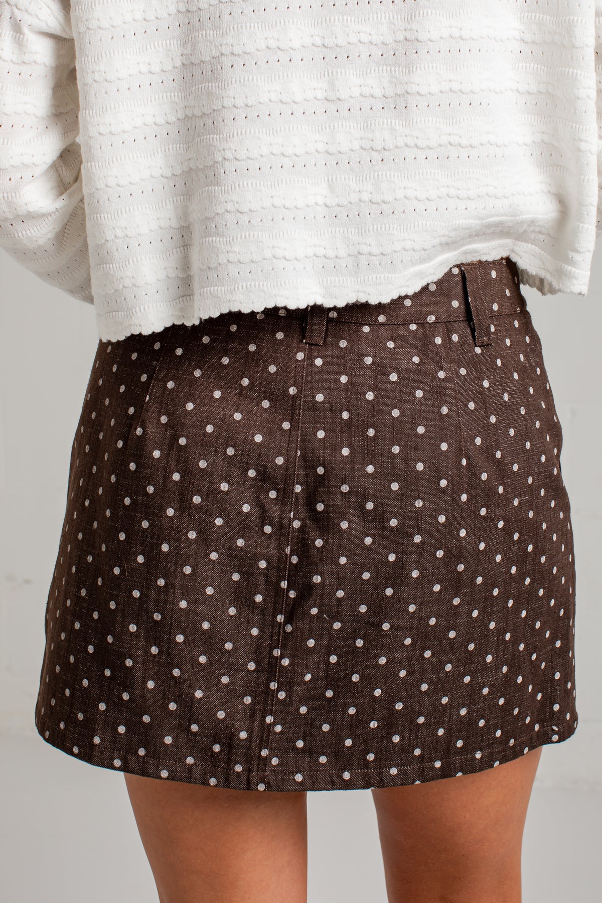 A close-up of a person wearing a brown skirt with a white polka dot pattern, paired with a white textured top.