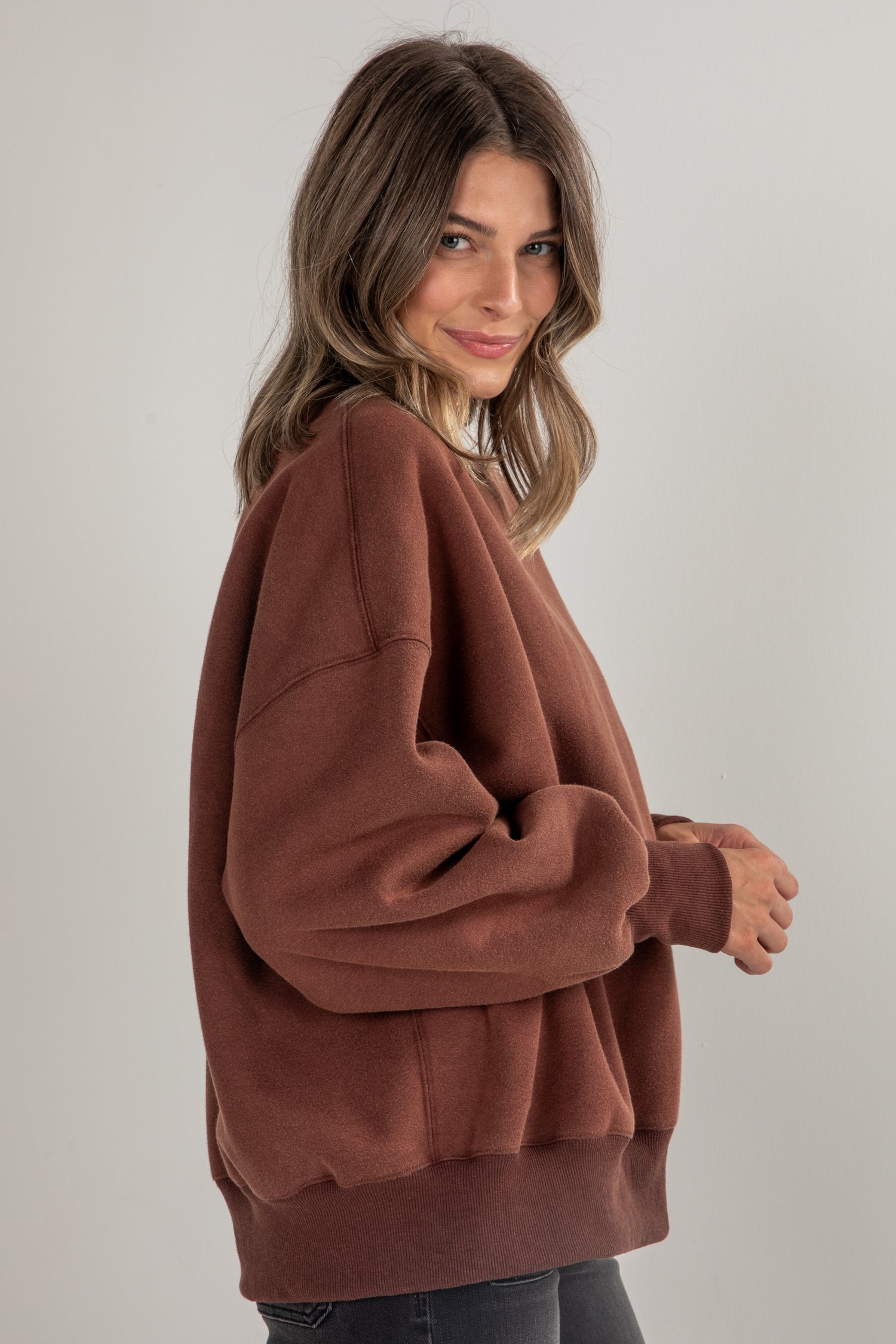 Woman wearing a brown oversized sweater against a plain background