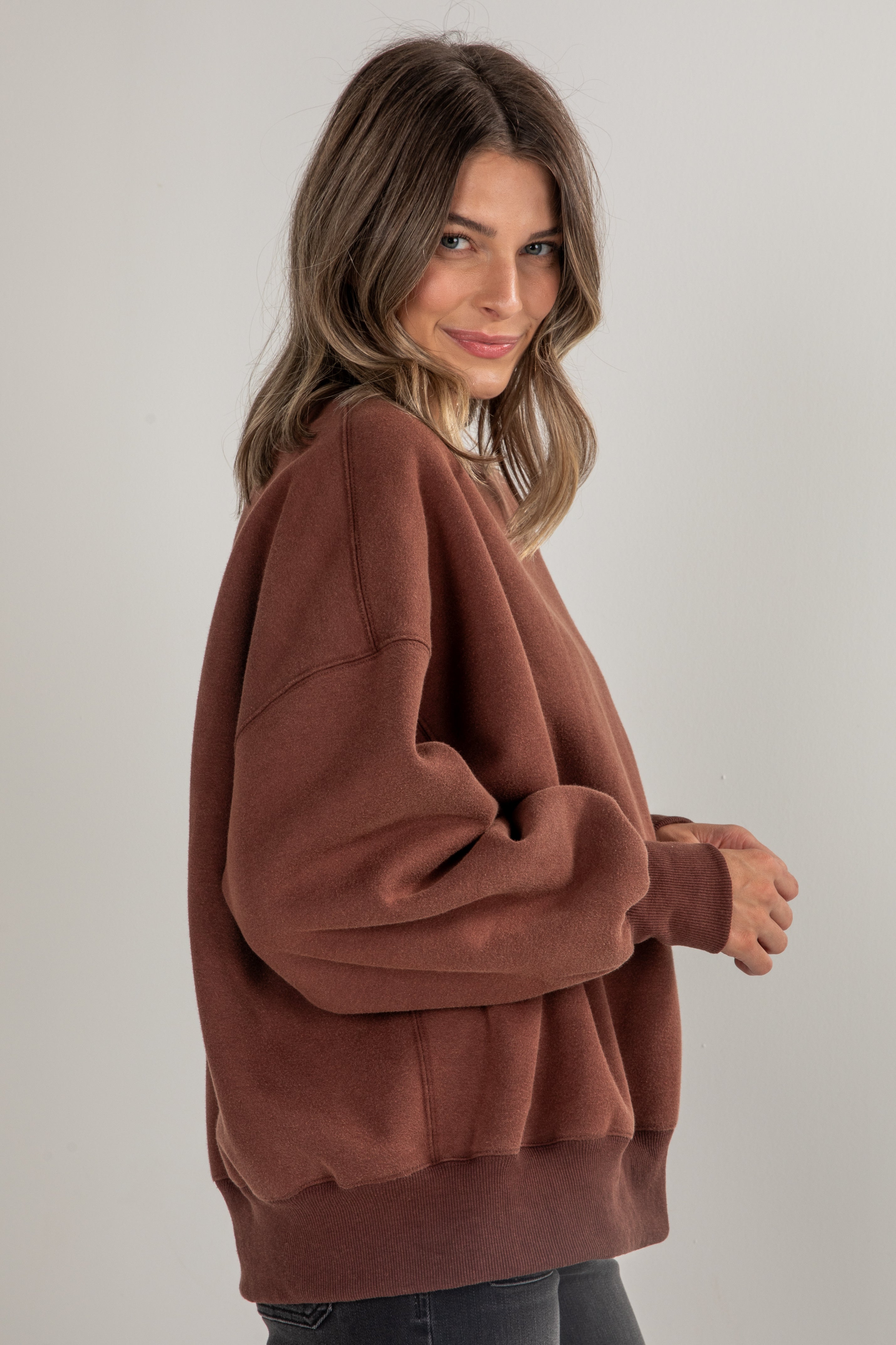 Woman wearing a brown oversized sweater against a plain background