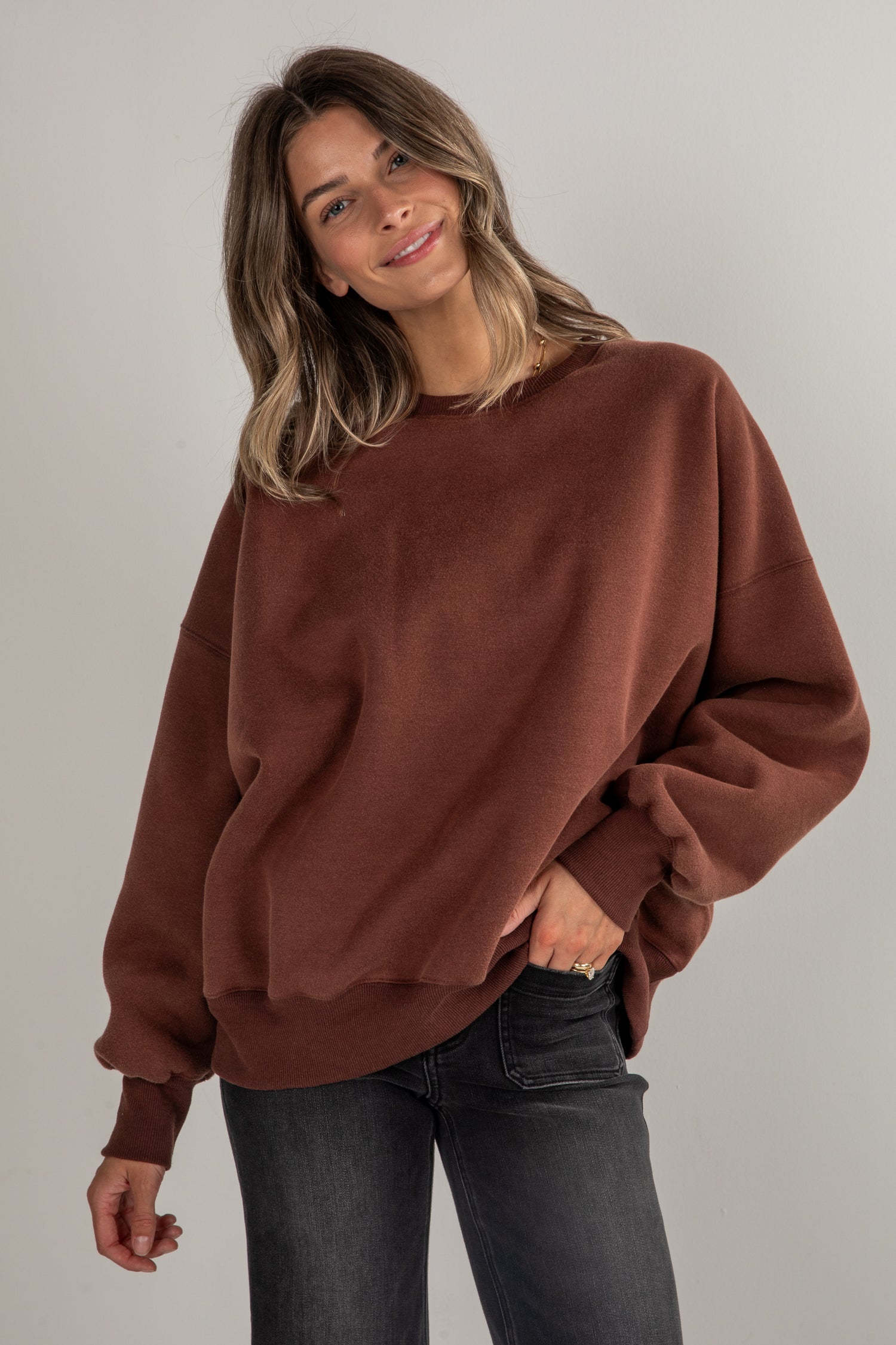 Woman wearing a brown sweatshirt and black jeans against a plain background