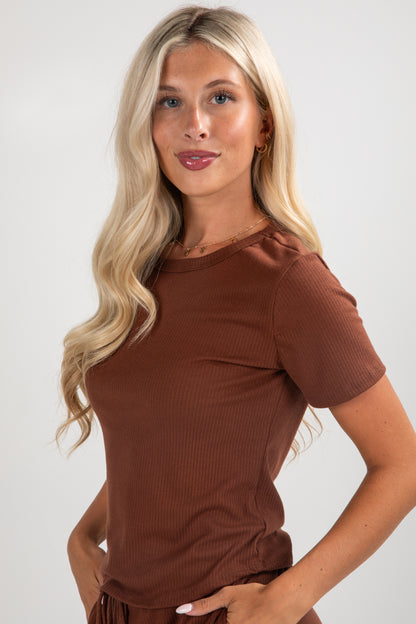 Woman wearing a brown top with ruffled sleeves against a white background