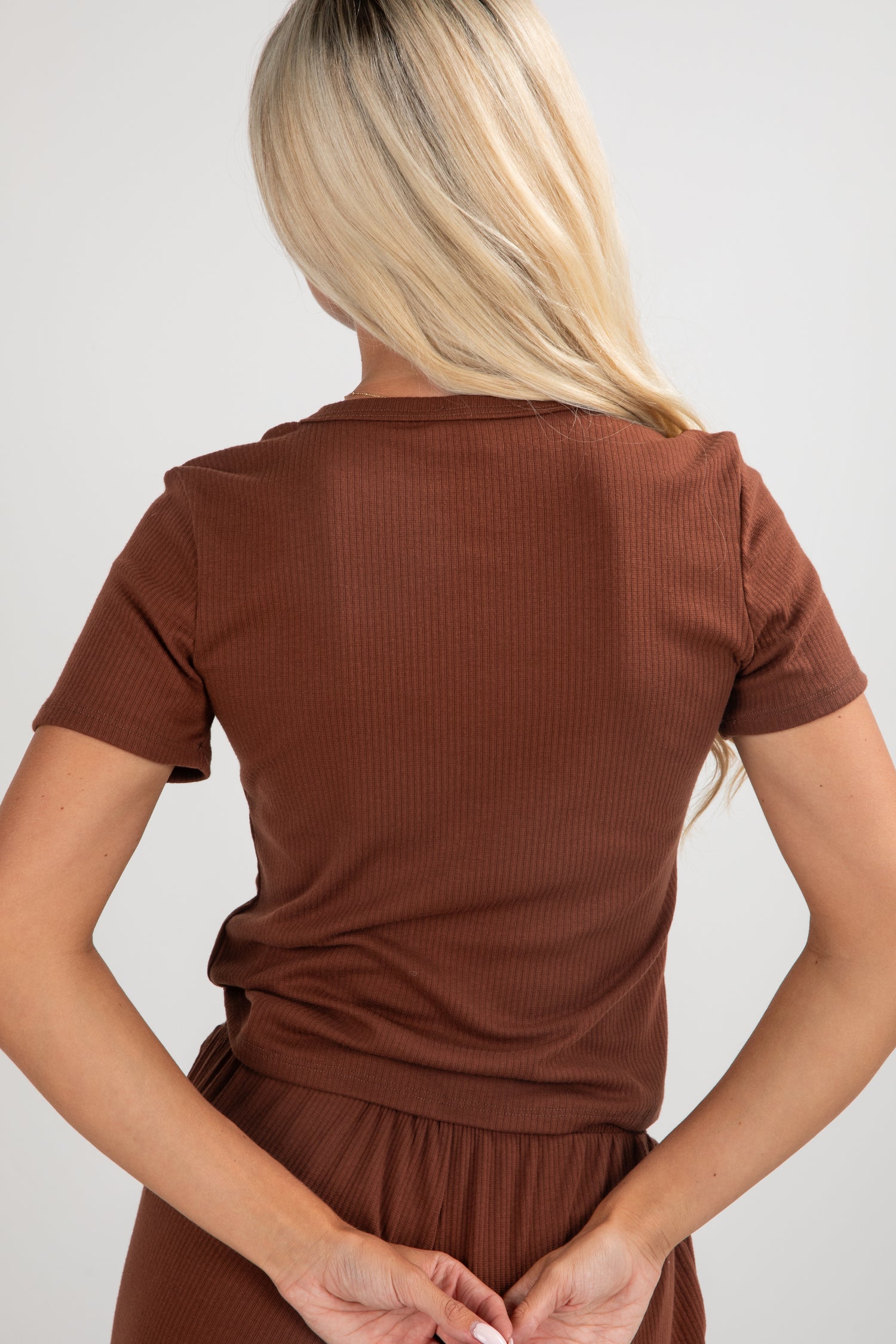 Person wearing a brown ribbed top and pants on a plain background