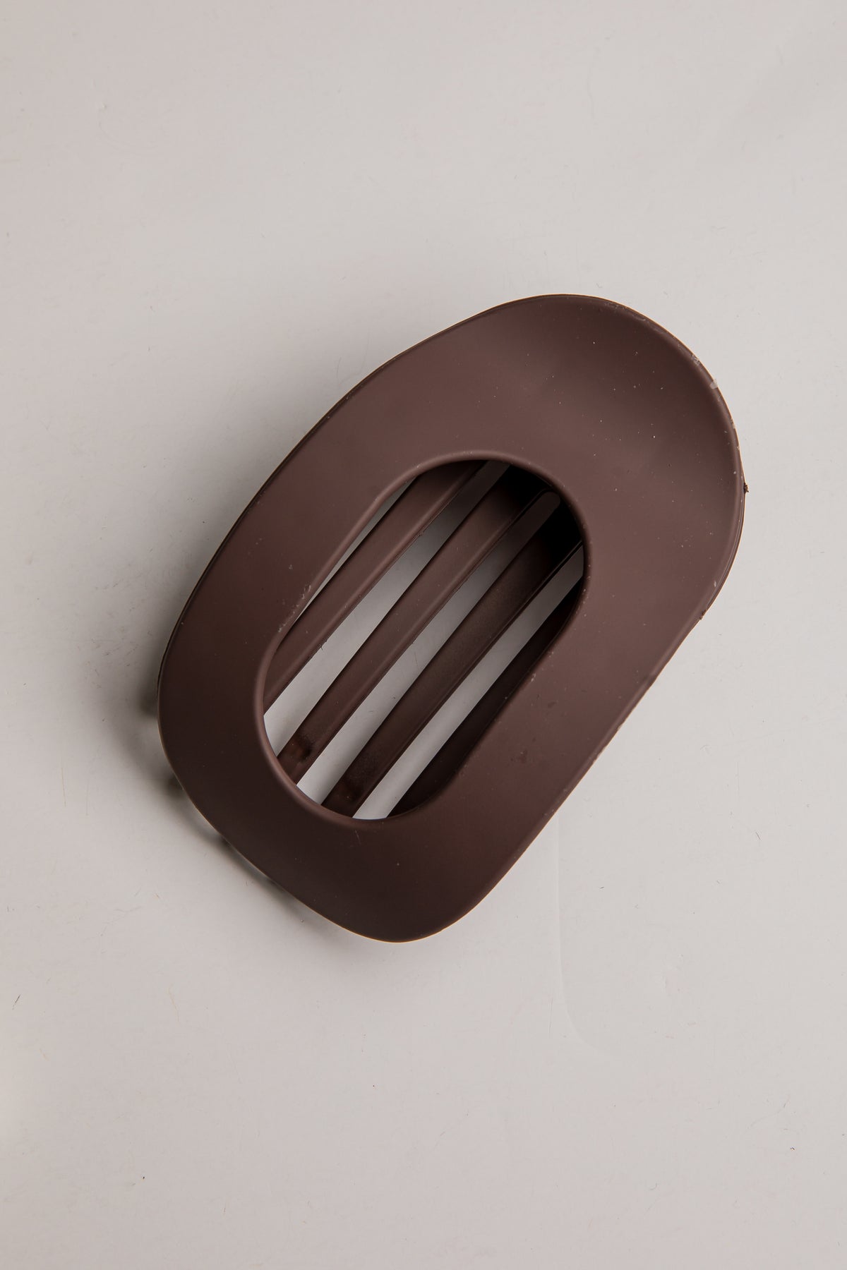 A dark brown silicone kitchen accessory, likely a lid protector or guard, with a slotted oval design, shown on a neutral light gray background.