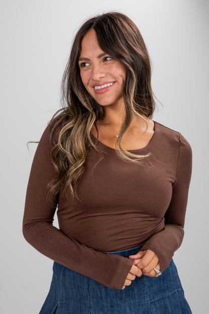 Woman wearing a brown long-sleeve top and blue skirt against a gray background