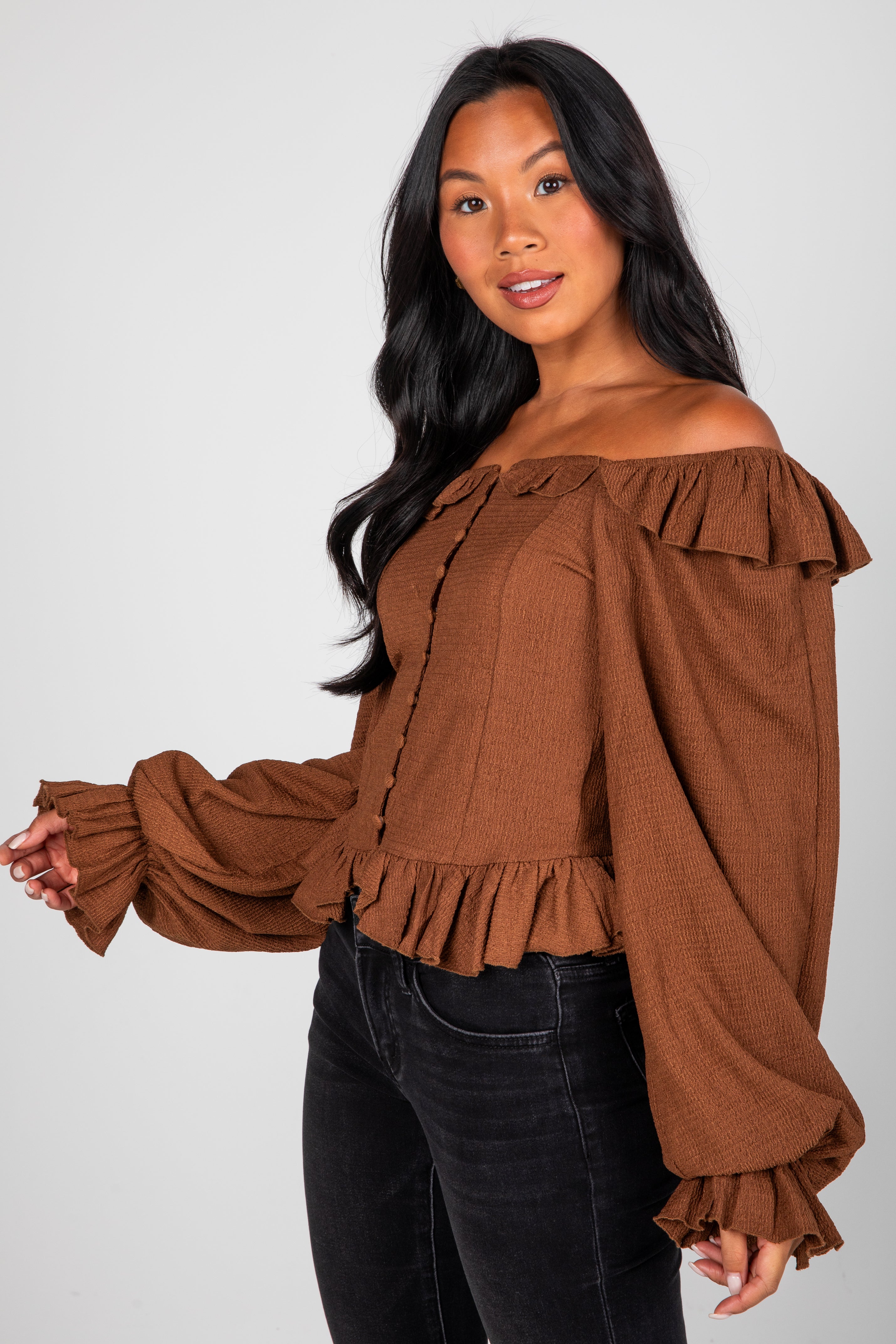 Woman wearing a brown off-shoulder blouse with ruffled details on a white background