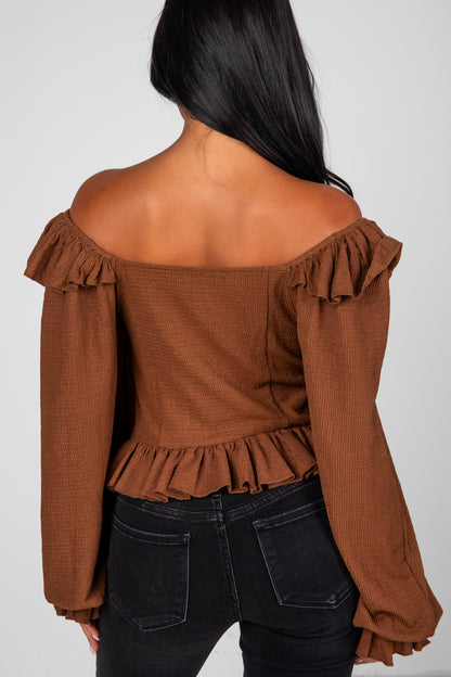 Brown off-shoulder top with ruffled details worn by a person on a plain background