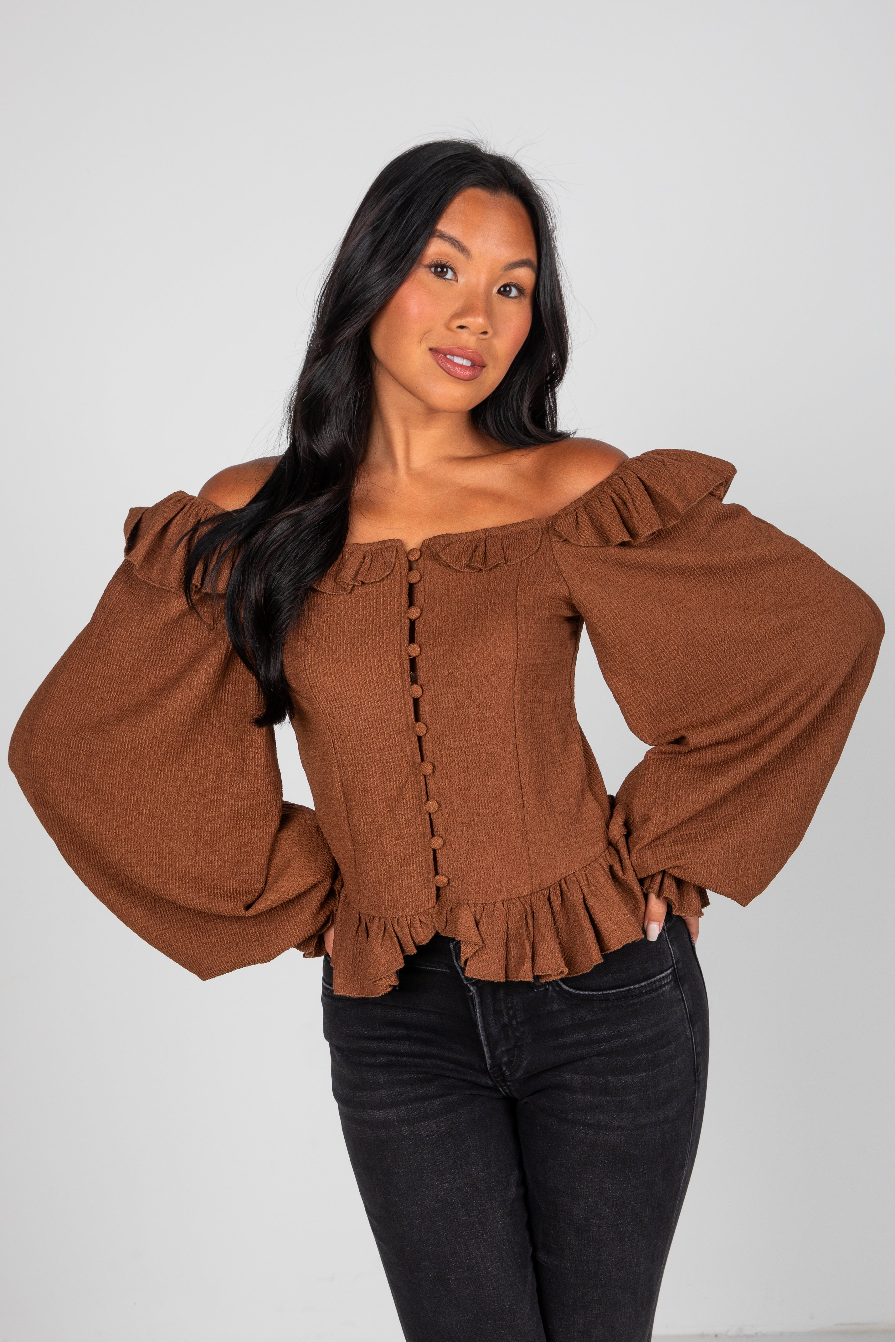 Woman wearing a brown off-shoulder top with puffed sleeves on a white background