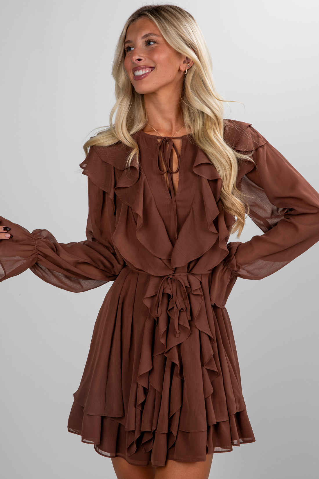 Woman wearing a brown ruffled dress against a plain background