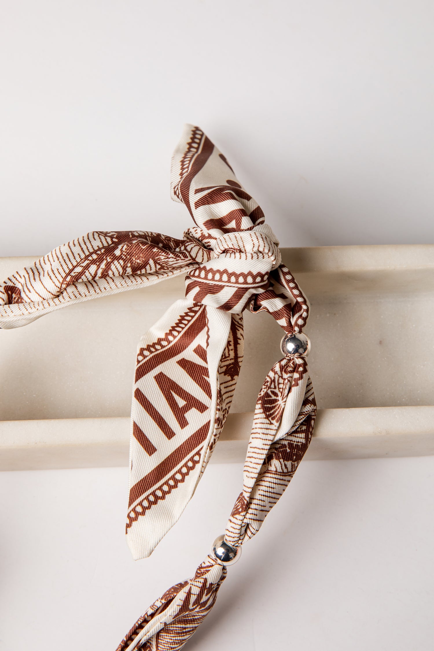 Brown and beige patterned headband with decorative elements on a white surface